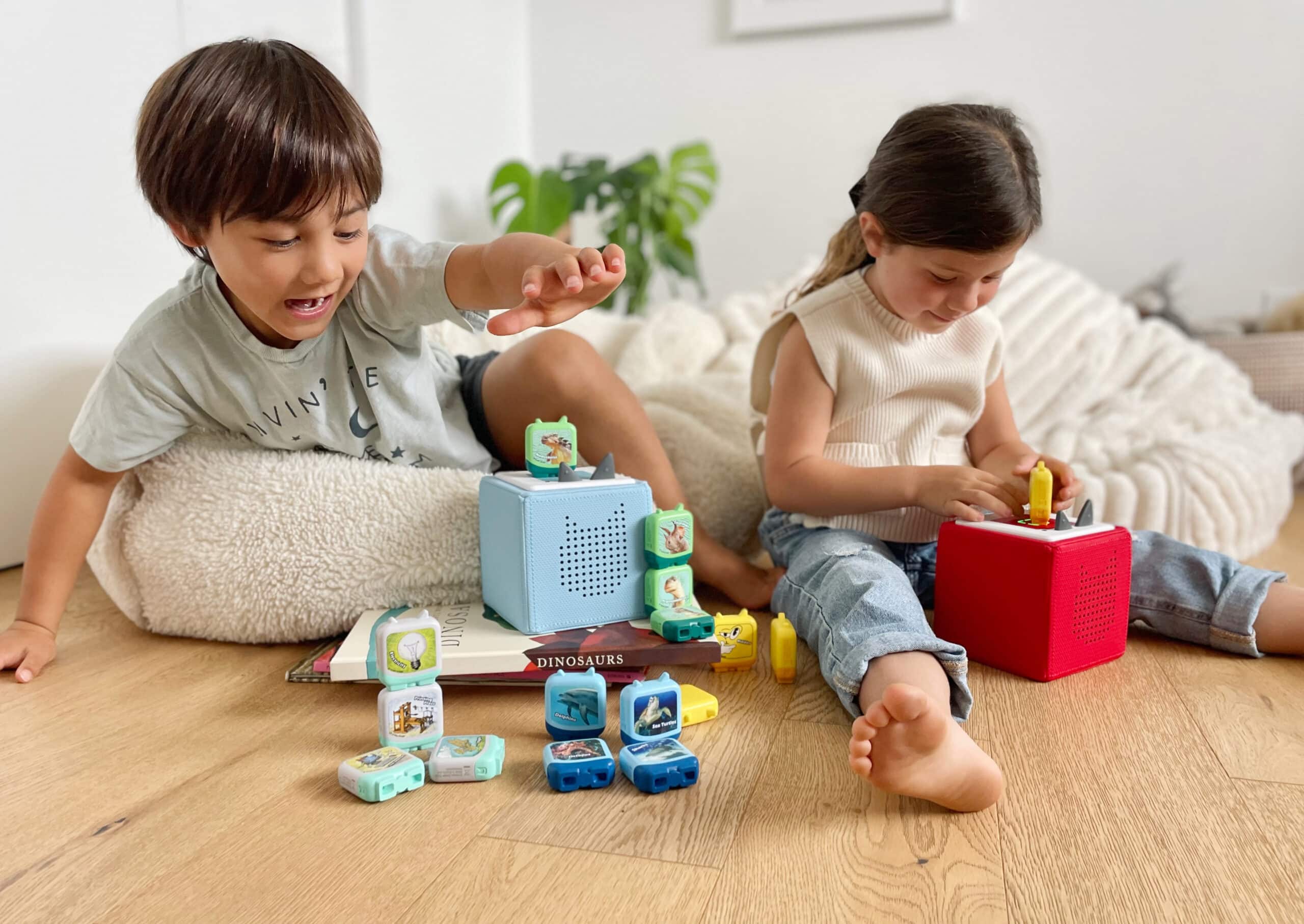 Zwei Kinder sitzen in einem Kinderzimmer und hören Tonies auf ihren Tonieboxen.