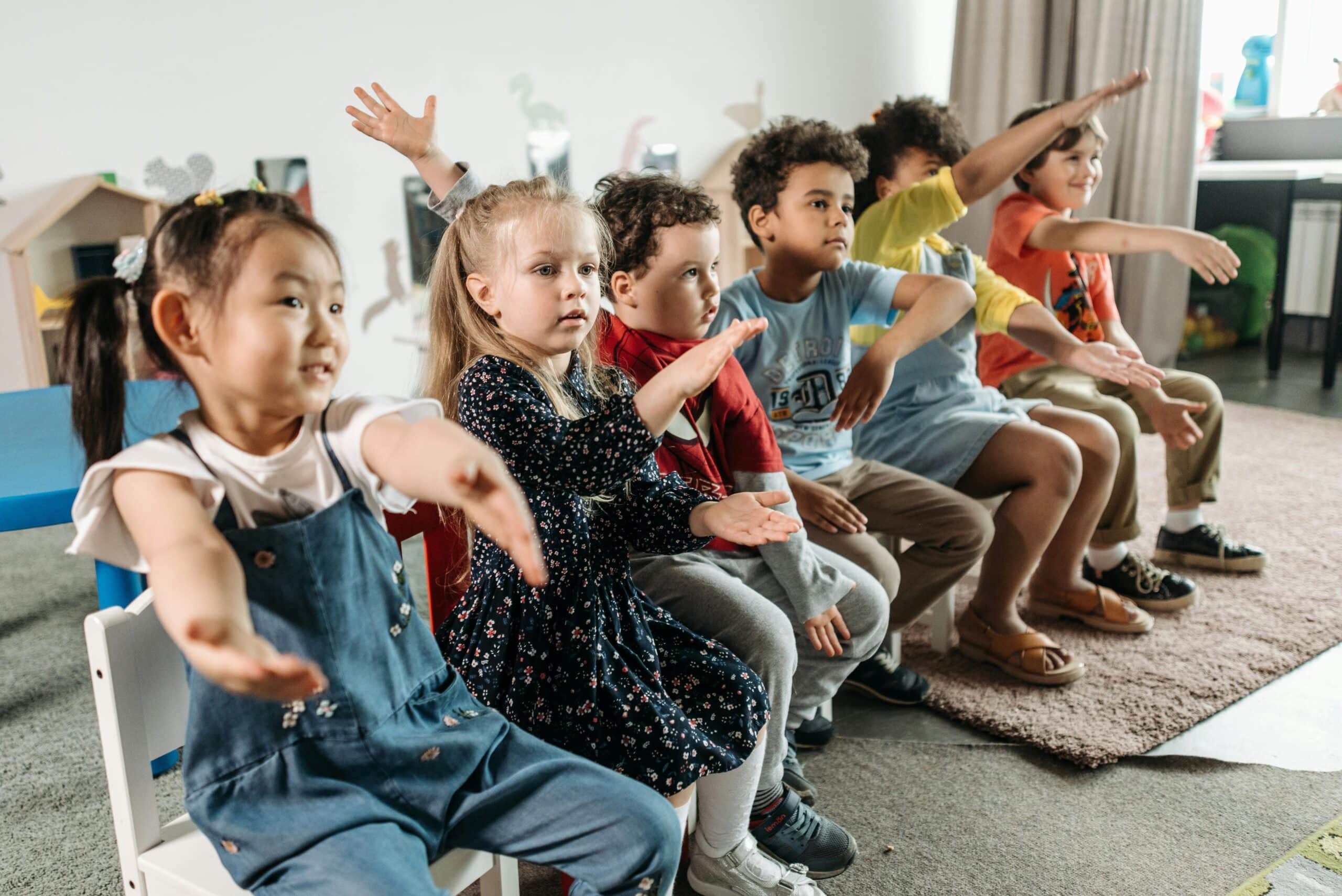 Kinder spielen auf Stühlen ein Mitmachspiel, bei dem sie ihre Arme bewegen müssen